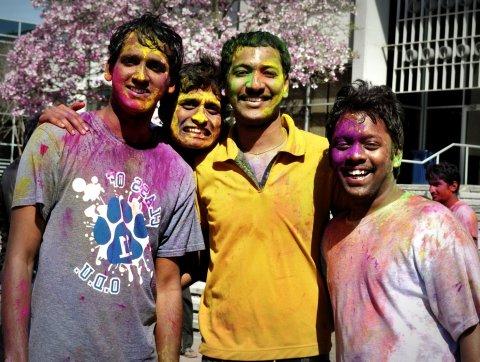 Four students covered in brightly colored powder celebrating Holi Festival.